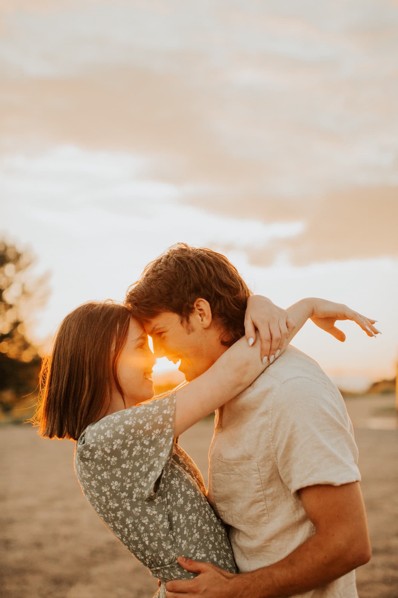 A couple touch foreheads, backlit by a low golden sun