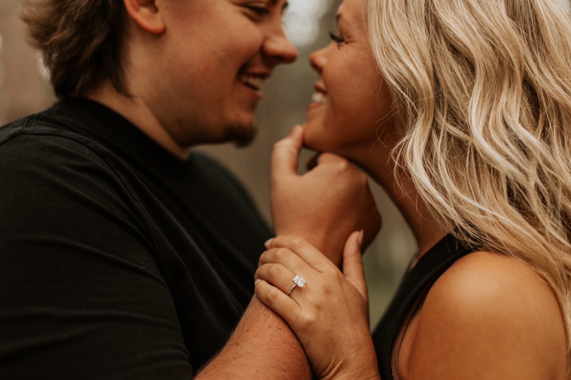 A close-up of an engaged couple smiling nose to nose, her hand on his cheek showing her engagement ring