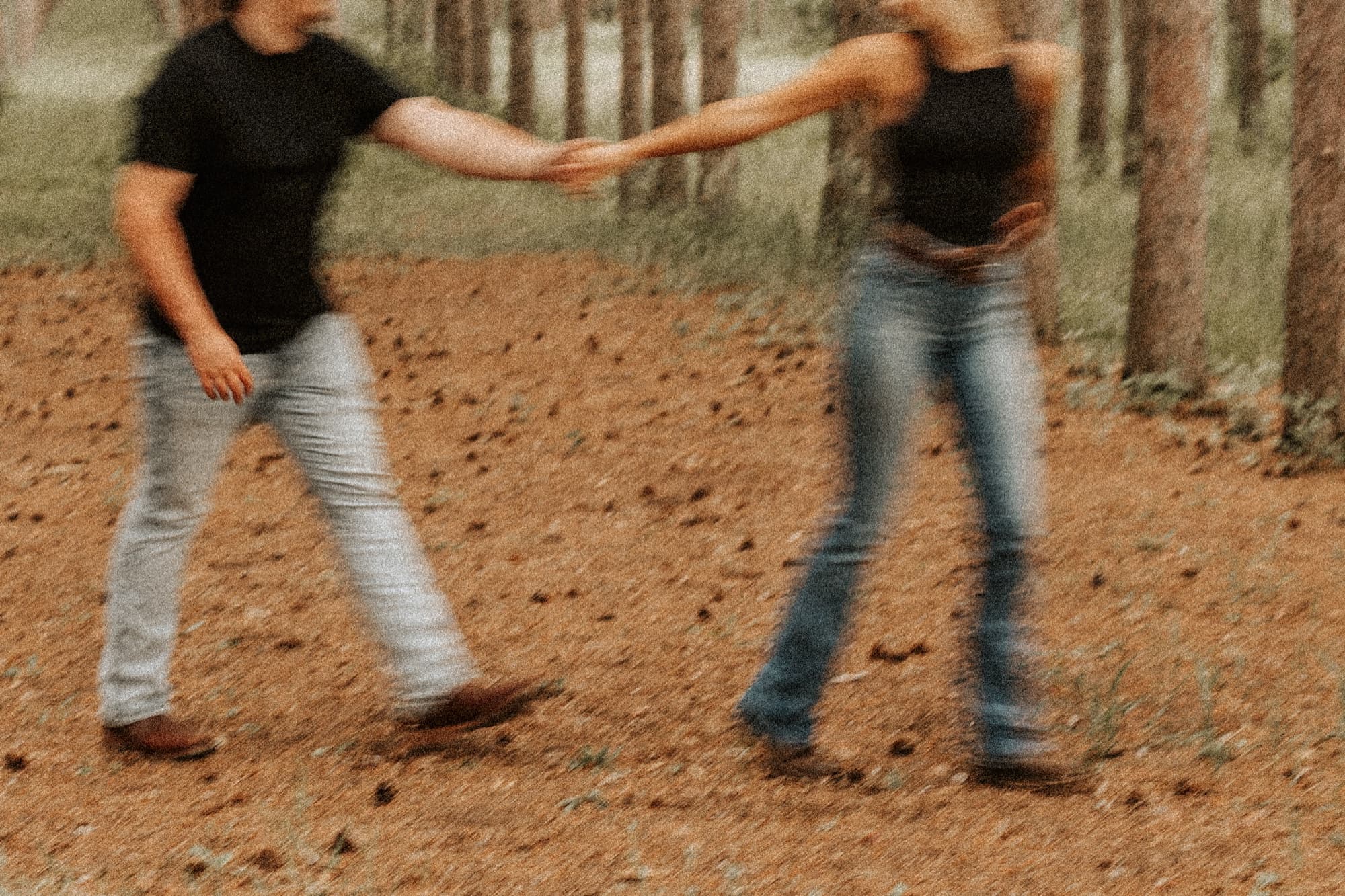A couple spin hand in hand through a pine forest, blurred with motion