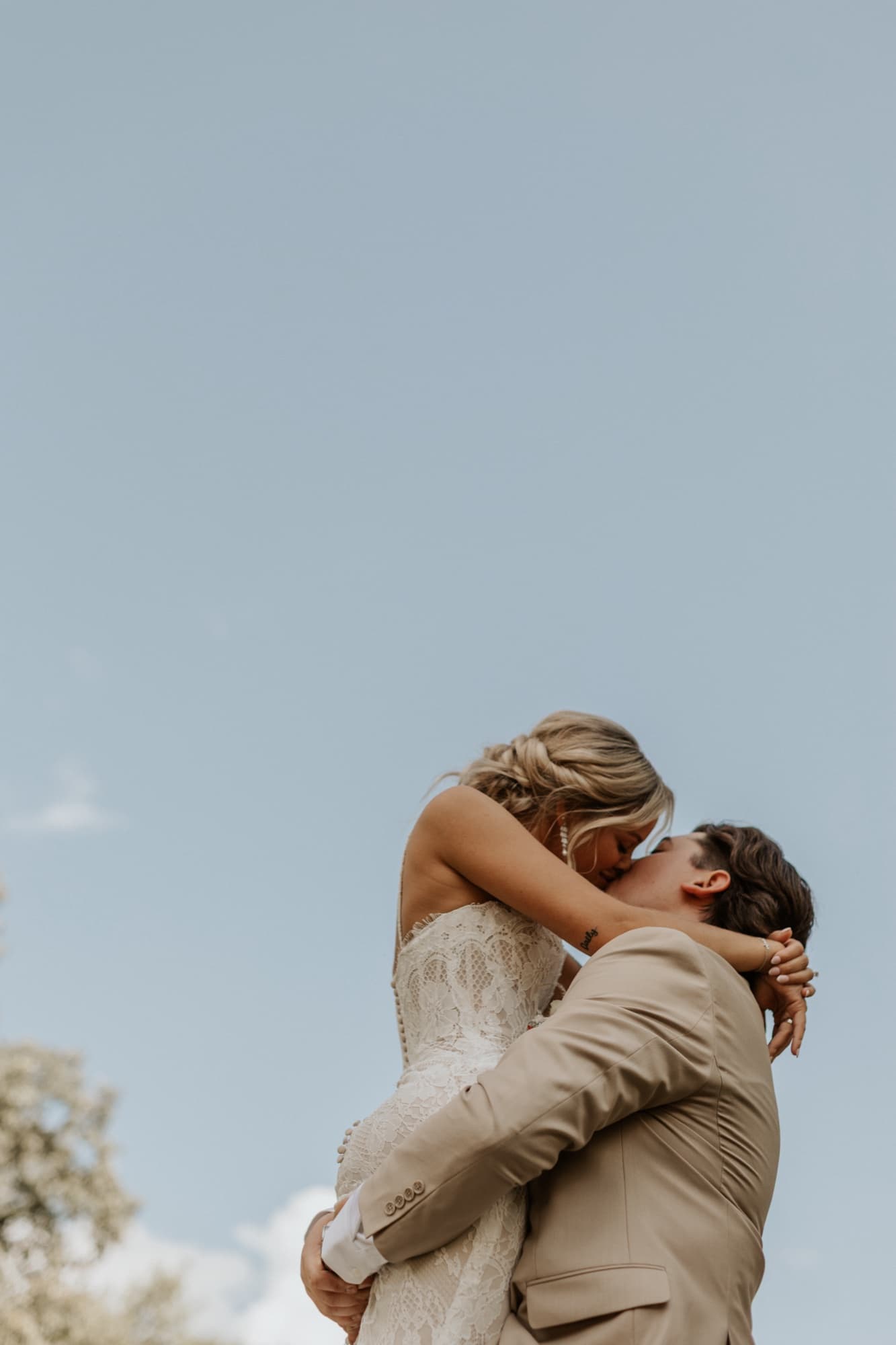 Caleb lifts Betsy into a kiss against a clear blue sky