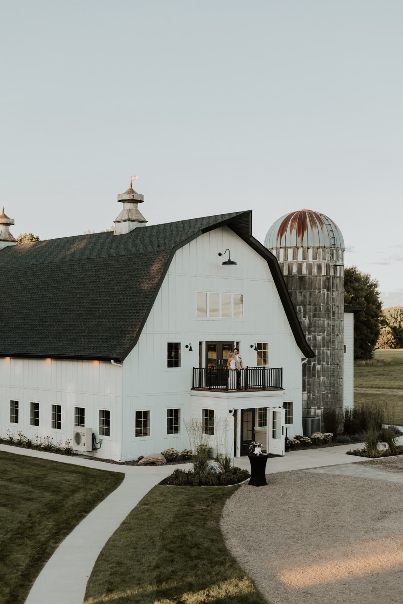 A white barn venue with a rusted silo, the newlyweds standing together on its small upper balcony