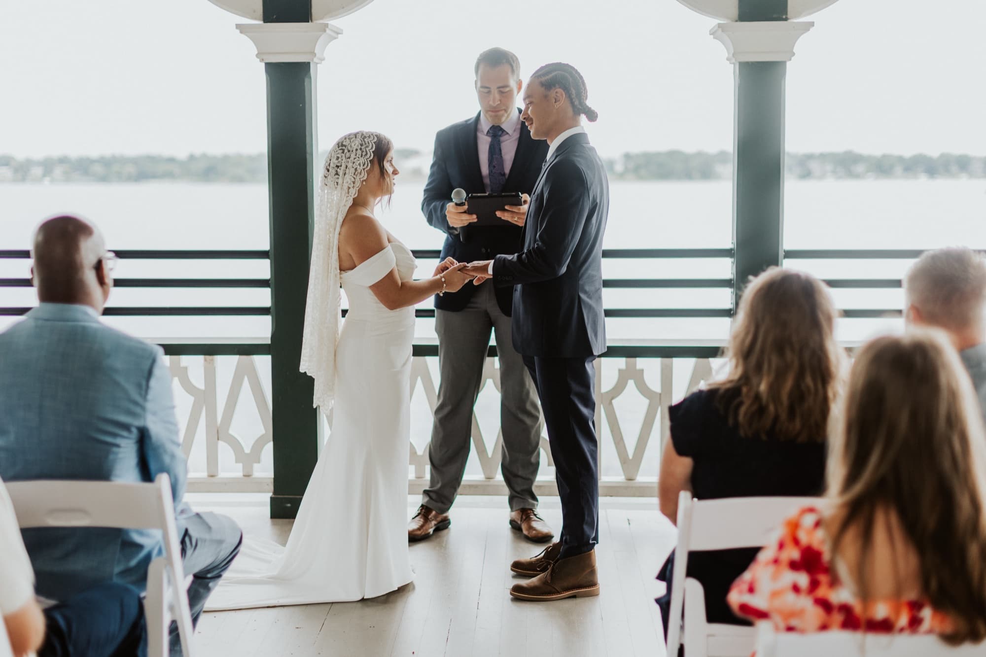 Nic and Tirzah hold hands facing their officiant in the gazebo, the lake stretching out behind them