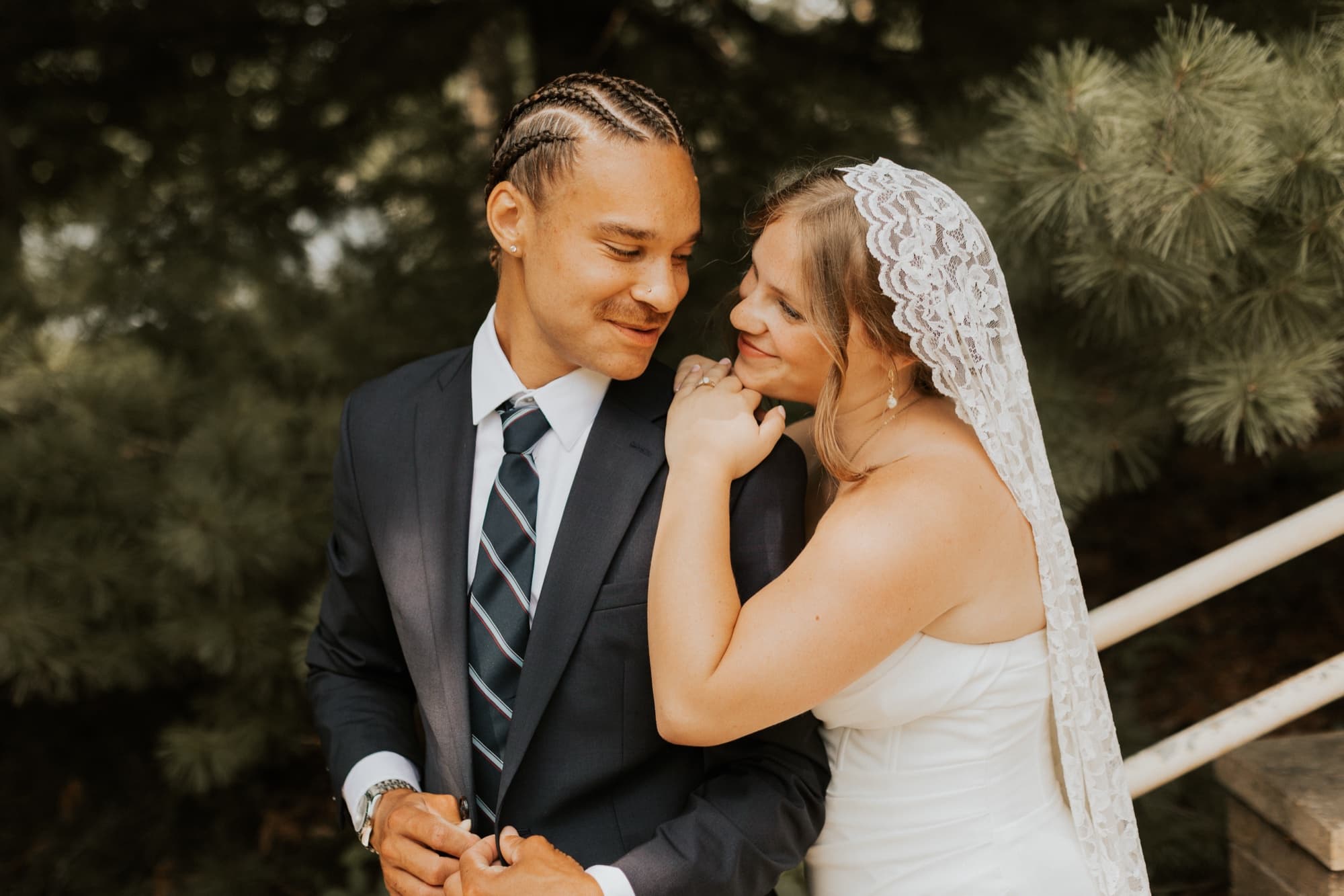 The bride rests her chin on the groom's shoulder and smiles, her lace veil framing her face